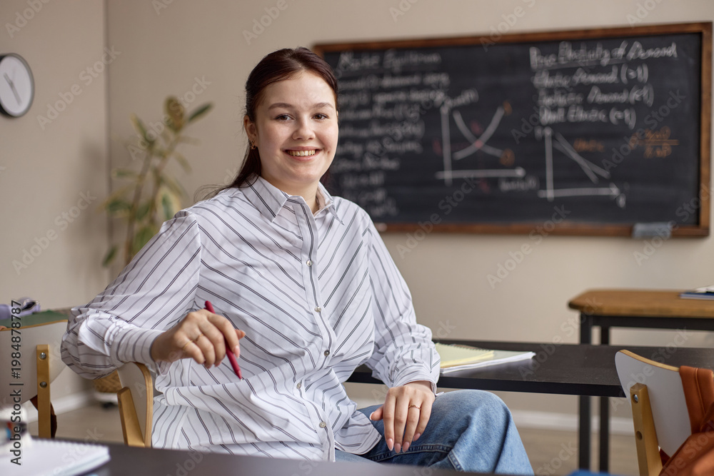 Ταπετσαρία Portrait of Caucasian young adult woman sitting in classroom, holding pen, smiling at camera with math board behind