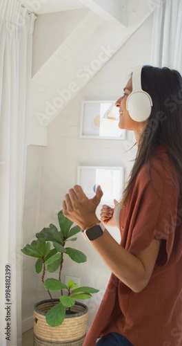 Vertical video: Woman by tall window, music starting, swaying and adjusting white headphones