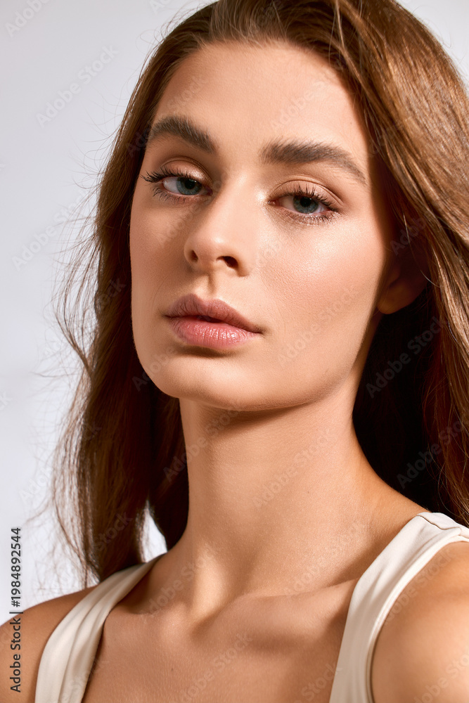 Obraz premium Elegant young woman exudes chic beauty with a serene expression in a soft lit setting.
