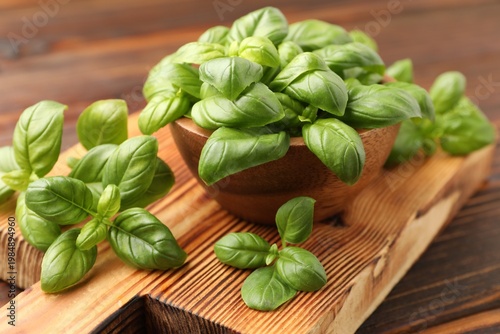 Fresh basil leaves and bowl on wooden table, closeup