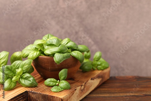 Fresh basil leaves and bowl on wooden table against grey textured background, closeup. Space for text