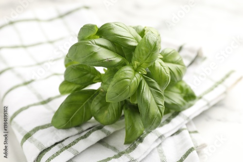 Fresh basil leaves and checkered napkin on white table, closeup