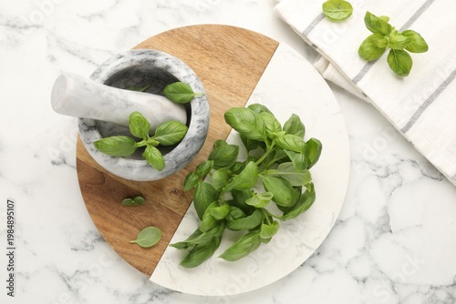 Fresh basil leaves, mortar and pestle on white marble table, flat lay
