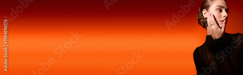 Valokuva Elegant young woman showcasing sophisticated style against a vibrant orange background