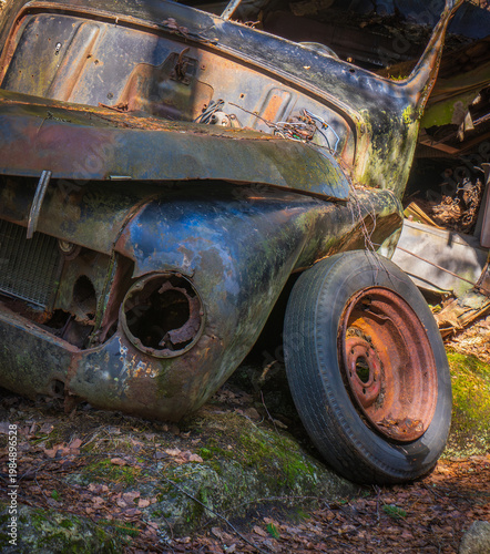 Abandoned vintage car with missing headlight and rusted wheel in forest