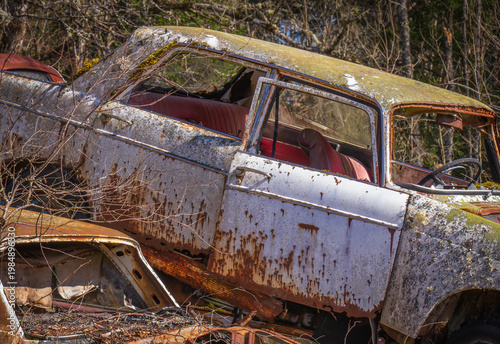 Abandoned vintage car with missing headlight and rusted wheel in forest