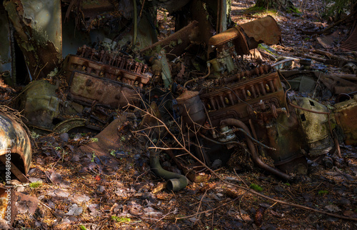 Abandoned vintage car with missing headlight and rusted wheel in forest