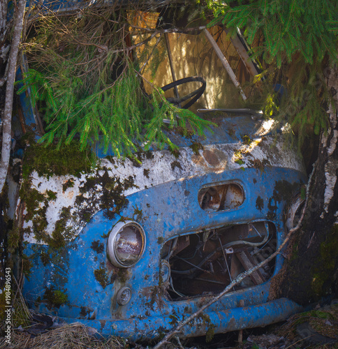 Abandoned vintage car with missing headlight and rusted wheel in forest