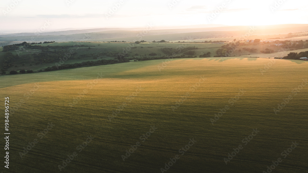 Fototapeta premium Golden hour illuminates vast agricultural fields and rolling hills at sunrise