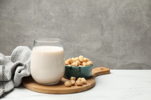 Fresh chickpea milk in glass and seeds on white marble table near grey wall, closeup with space for text. Vegan drink