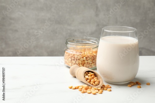 Fresh chickpea milk in glass and seeds on white marble table near grey wall, closeup with space for text. Vegan drink