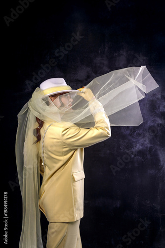 High fashion photography: a beautiful, elegant woman in a yellow pantsuit posing against a dark background. Slim figure. Hair cut and styled. Studio shot. The model is seated on a chair.