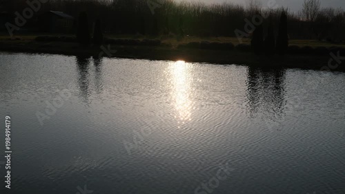 Brilliant sun reflection shimmers and ripples across a pond surface.