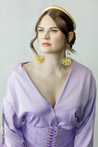 A beautiful, elegant woman in a lilac dress, bright green neon boots, and a handbag posing against a light background. Slender figure. Hair cut and styled. Studio shot. The model is seated on a chair.