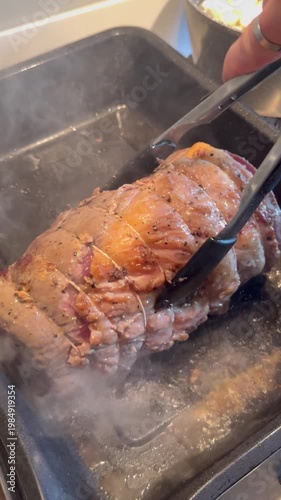 Vertical video social media - Closeup of a hand using a pair of tongs to turn a raw topside joint of beef, searing in juices, inside a smoking hot oven baking tray, before the main oven cooking.