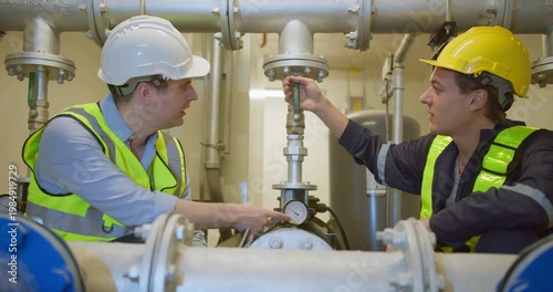 Two industrial engineers collaborating on system diagnostics, inspecting the pipeline and pressure gauges during a maintenance check in a factory plant room.