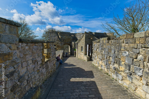 Obraz na plátne A historic stone pathway between castle walls leads towards archways under a blue sky