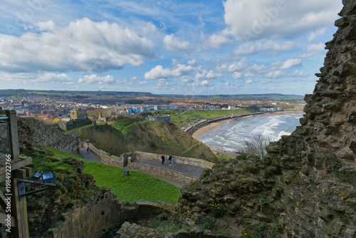 A scenic view from castle ruins overlooking a coastal town, beach, and ocean under a cloudy sky in Scarborough Castle - Yorkshire - Great Britain