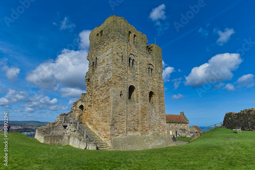 A large, weathered stone castle ruin stands on a green hill under a bright blue sky with white clouds in Scarborough Castle - Yorkshire - Great Britain