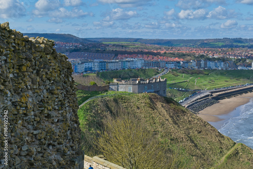 Placeholder
A scenic view features ancient castle ruins atop a hill. Below, a coastal town stretches alongside a beach and the sea in Scarborough Castle - Yorkshire - Great Britain