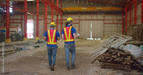 Two engineers in safety gear are inspecting an industrial warehouse, surveying the construction site for a new development or renovation project.