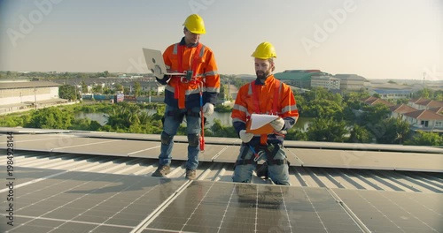 Two solar technicians collaborate on a rooftop, using a laptop and clipboard to perform system diagnostics and quality control on a photovoltaic installation.