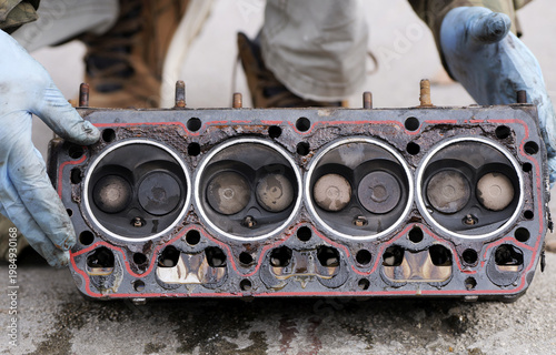 Photos Disassembled cylinder head with combustion chambers facing up, showing valves and gasket area, with gloved hands pointing to sealing issues and wear