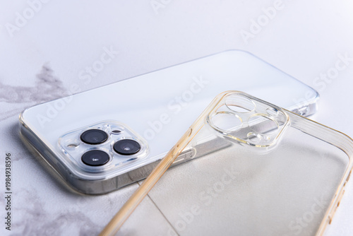 Old dirty silicone and new transparent phone cases on smartphone on marble background.