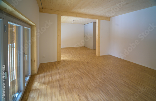 Brightly lit empty room with wooden floor in empty apartment, minimalist interior design, modern architecture in natural light