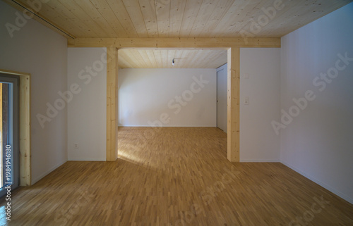 Brightly lit empty room with wooden floor in empty apartment, minimalist interior design, modern architecture in natural light