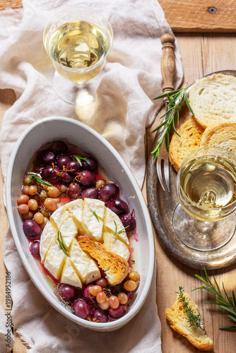 Baked Camembert cheese with grapes, thyme, and rosemary, served with white wine and a baguette.