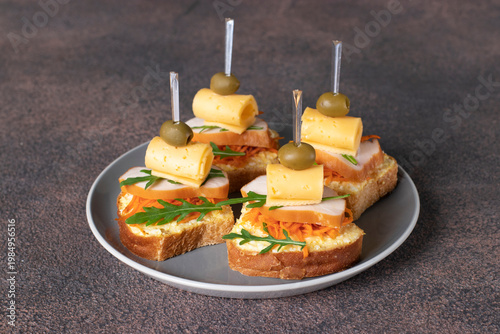 Festive canapes with smoked chicken, carrot, cheese, green olives and arugula on gray plate