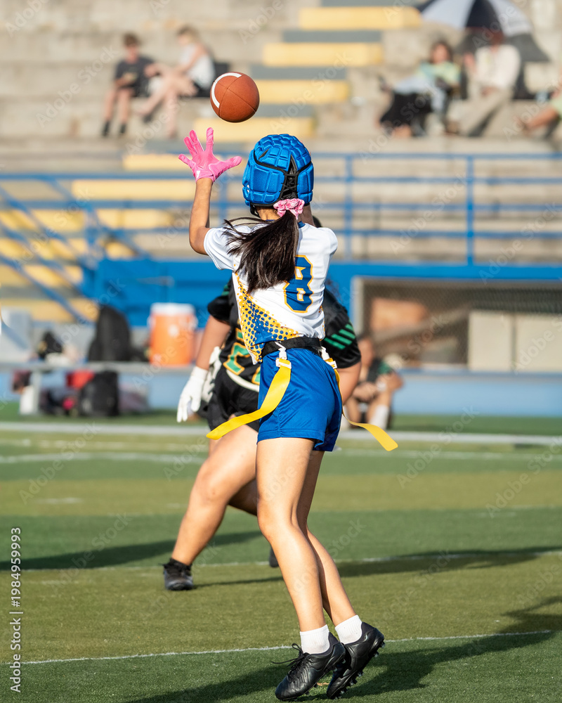 Fototapeta premium Girls flag football receiver leaps for a high pass while closely defended during a competitive outdoor game.