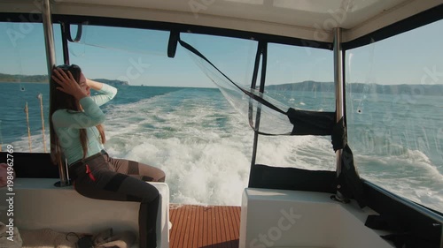 Young beautiful woman sits on stern of yacht and admiring views of bay with mountain ranges on coast. Slow motion.