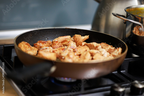 Frying small pieces of chicken meat in a pan on a gas stove