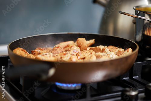 Frying small pieces of chicken meat in a pan on a gas stove