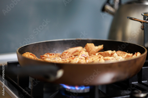 Frying small pieces of chicken meat in a pan on a gas stove