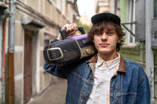 Retro fashion portrait young man with portable radio on shoulder, streetwear style, eighties revival, urban music culture, confident youth identity.
