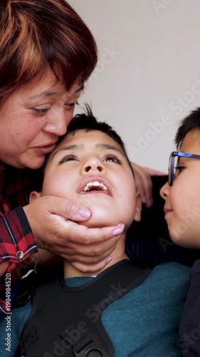 Happy latin american mother kissing her diverse children at home - Family love and disability care concept - Vertical video - ugc content