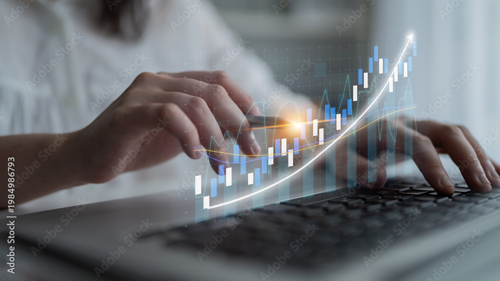 Fototapeta premium A focused individual types on a laptop, with a dynamic financial chart overlay representing growth and analysis in business and investment strategies. Impute