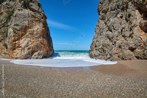 Scenic view of massive rock cliffs bordering a wild Mediterranean beach with sea foam. Iconic natural landmark for European travel marketing and coastal vacation campaigns. Spectacular seaside scenery