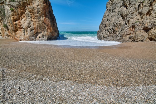 Scenic coastal gorge opening to a wild beach with crashing sea waves. Famous natural landmark in Europe for Mediterranean vacation advertising and travel brochures. Spectacular seaside scenery.