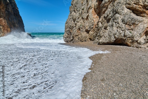 Scenic coastal gorge opening to a wild beach with crashing sea waves. Famous natural landmark in Europe for Mediterranean vacation advertising and travel brochures. Spectacular seaside scenery.