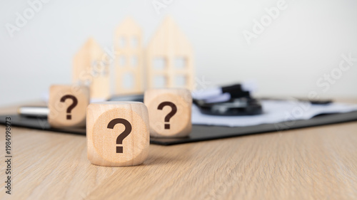 Question marks on wooden blocks. Blurred background with miniature houses, magnifying glass and documents. Real estate FAQ concept.