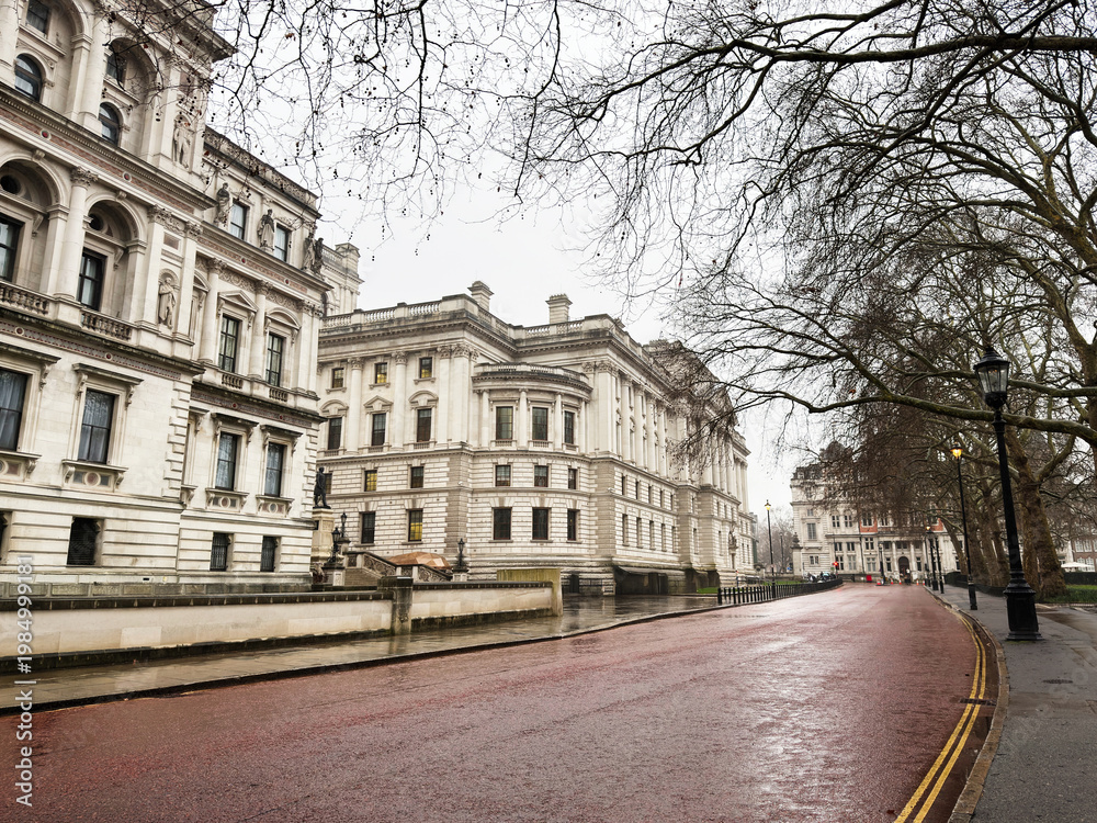 Fototapeta premium London street scene with historic buildings, wet pavement, and people under umbrellas