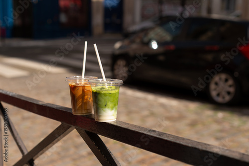 Принти на полотні Iced matcha latte and iced coffee in plastic cups with white straws on a black metal railing