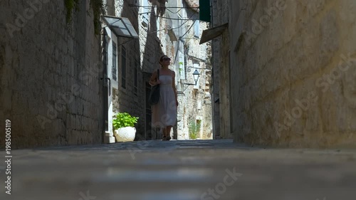 Woman walking down narrow old european street. Tourist woman in a summer dress walking along a narrow cobblestone alley in a historic old european town, enjoying her vacation and sightseeing