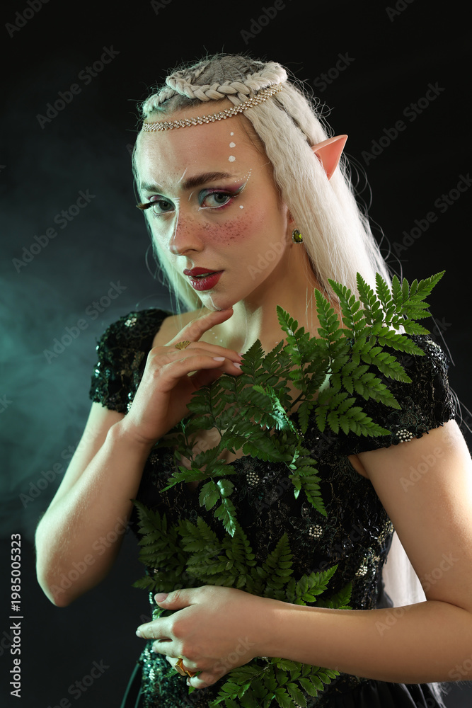 Fototapeta premium Beautiful elf girl with floral decor on black background with smoke