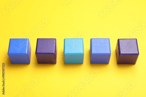 Empty colorful wooden cubes on yellow background, above view. Space for text