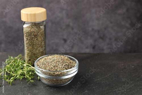 Dried thyme in glass jar, bowl and fresh leaves on black table, closeup. Space for text